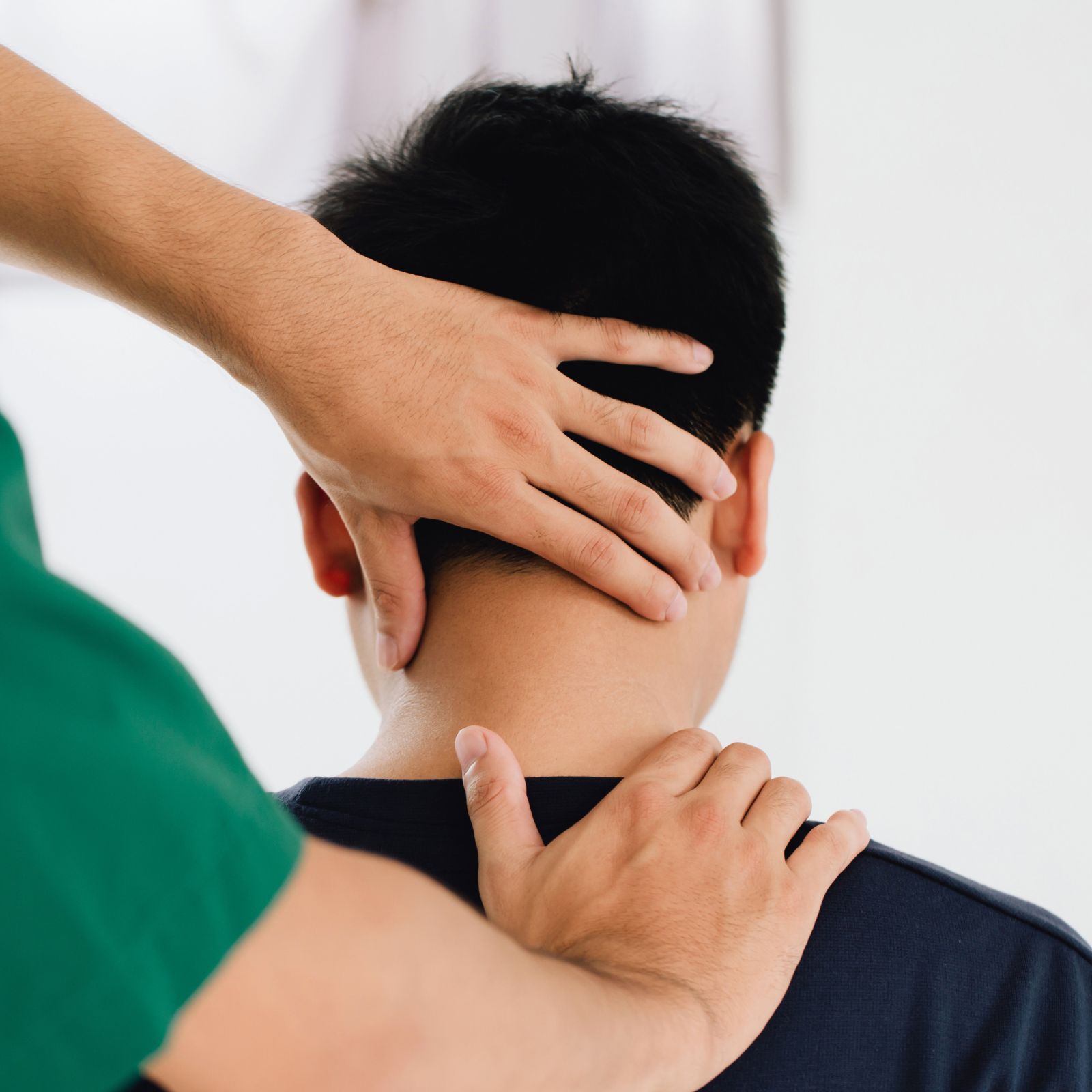 A healthcare professional adjusts a patient's neck with one hand while gently resting the other on their shoulder.