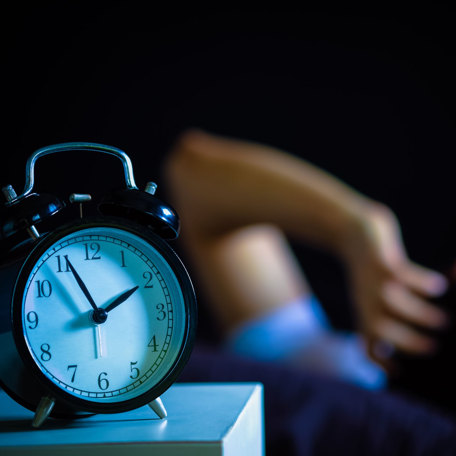 Analog alarm clock in focus with a blurred person in the background.