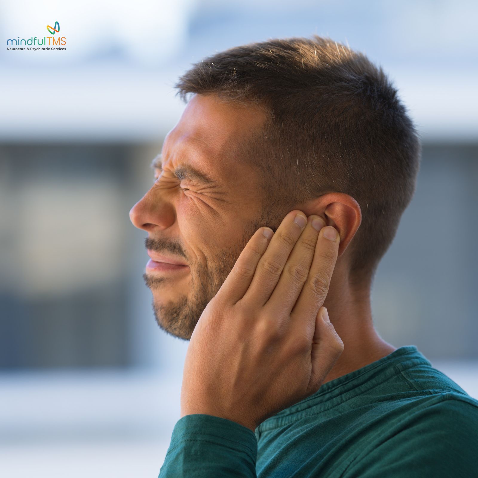 Person in teal shirt plugging their ear, logo "mindfulTMS" in corner.